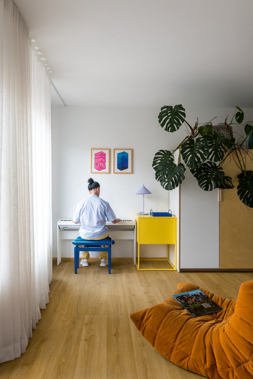 Klickvinyl Quick Step Bloom Botanic Smoked Oak im Wohnzimmer verlegt, orangefarbener Liegesessel, ein Mann sitzt auf einem Stuhl und spielt einen Synthesizer.