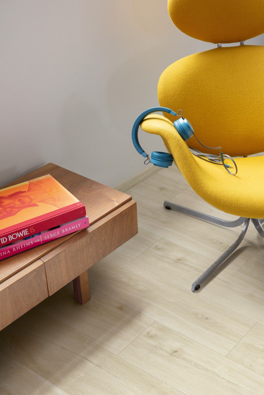 LVT põrandakate Quick-Step Blos Canyon tamm beige paigaldatud kodukontori põrandale. Kollane kontoritool millel sinised kõrvaklapid. Kummut millel on raamatud.