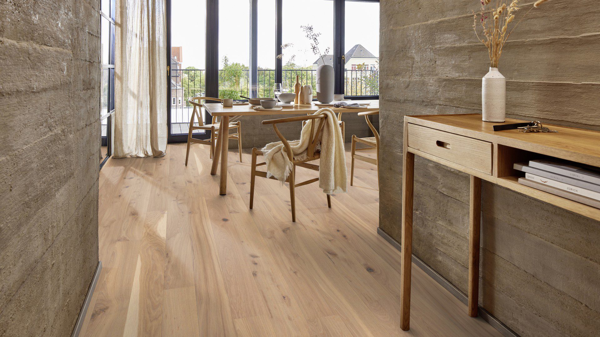 Fertigparkett Bauwerk Boen Casapark Eiche 46 Vivo (138 mm), gebürstet und mit Osmo Hartwachs-Öl geölt – verlegt im Flur und Essbereich; Holzesstisch mit Holzstühlen und gedecktem Tisch, rustikale Flurwände in Betonoptik. Rustikale Sortierung mit lebendiger Maserung und Astanteilen.