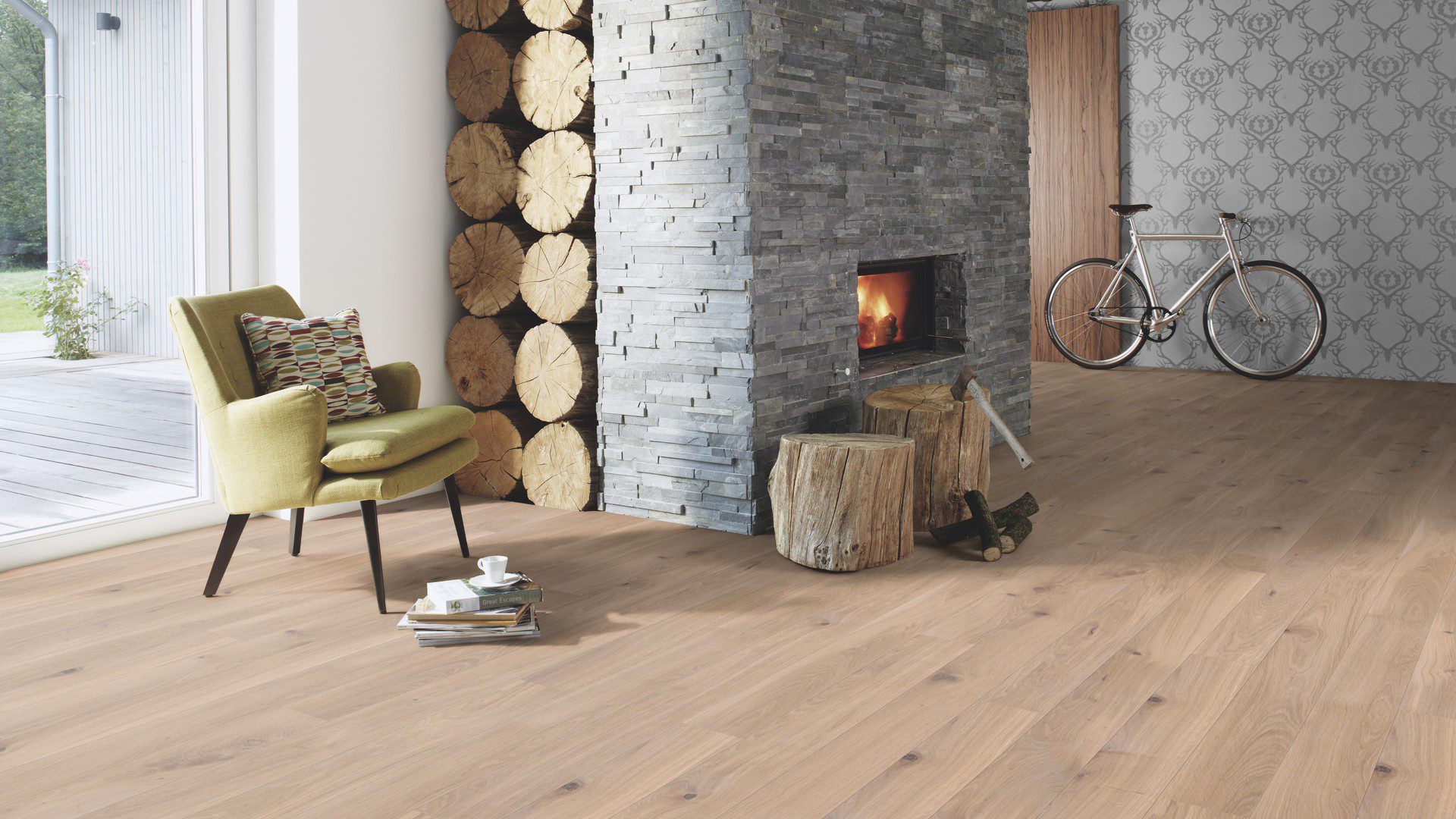 Lankkuparketti Bauwerk Boen Casapark tammi 46 Farina, harjattu ja öljyvahattu, asennettuna olohuoneen lattialle – suuri, harmaalla kivellä verhoiltu lämmitettävä takka, vihreä nojatuoli ja polkupyörä. Vaalea Farina-sävy ja rustiikkinen sorteerus tuovat esiin tammen eläväisen kuvioinnin.