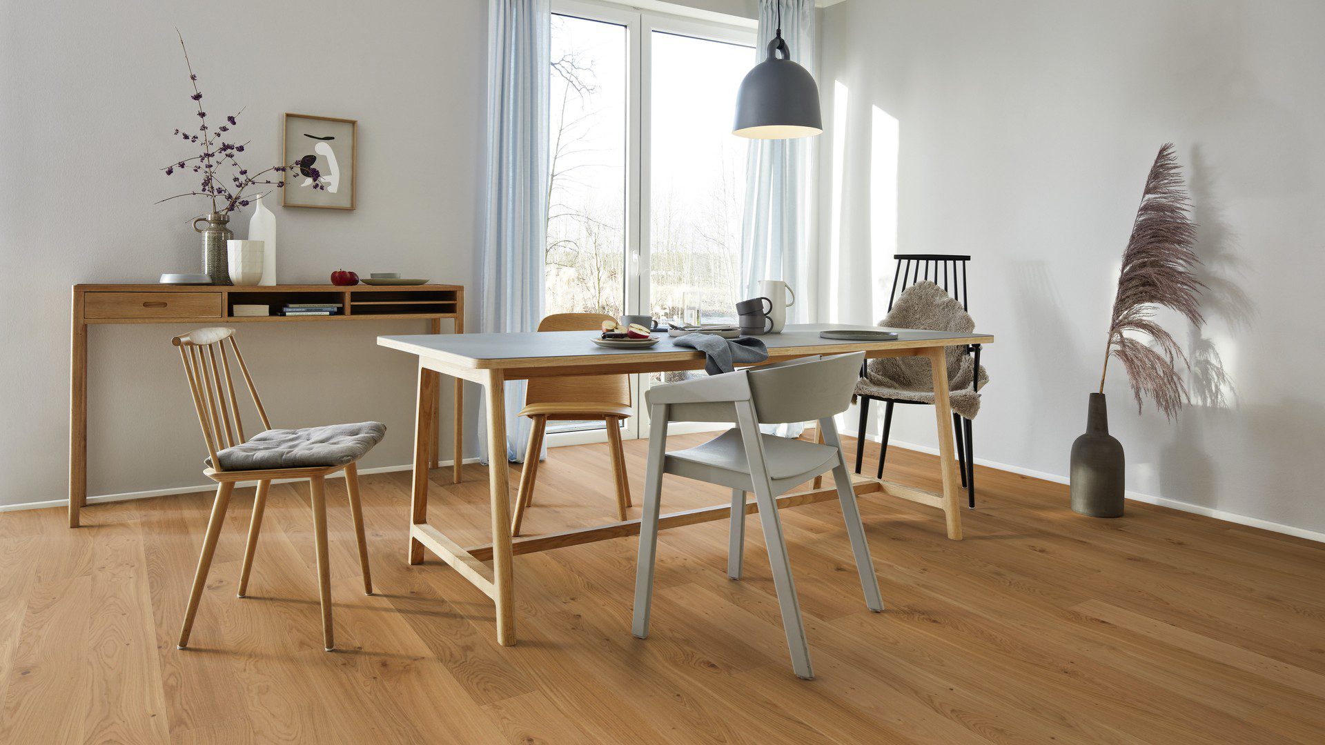 Lankkuparketti Bauwerk Casapark Budget Cut tammi 35, harjattu ja öljyvahattu, asennettuna ruokailutilan lattialle – ruokapöytä astioineen, tuolit pöydän ympärillä sekä seinän vieressä lipasto, jonka päällä on erilaisia vaaseja. Luonnollinen, lämminsävyinen tammensävy ja kevyesti rustiikkinen sorteerus (maltillisesti oksakohtia ja hienovaraista sävyvaihtelua).