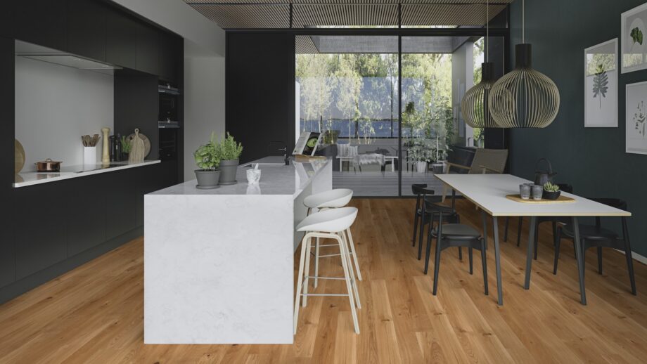 Parkettboden Bauwerk Casapark Eiche 46 (138 mm), gebürstet und matt lackiert, mit Fasen – verlegt auf dem Boden einer modern gestalteten Küche mit Küchenmöbeln, Kücheninsel und Esstisch; rustikale Sortierung mit lebendiger Maserung und Astanteilen.