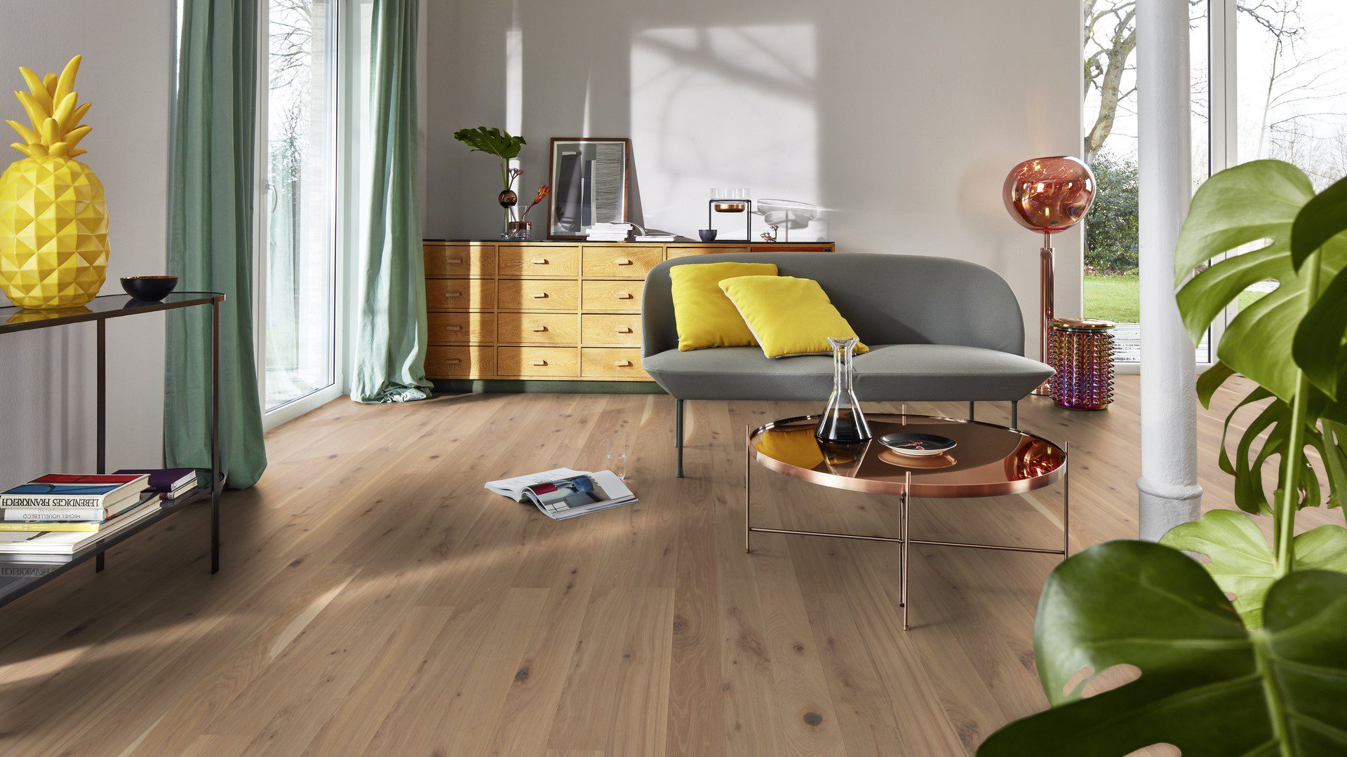 Tammiparketti Bauwerk Boen Casapark tammi 46 Vivo Avorio, harjattu ja öljyvahattu, asennettuna olohuoneen lattialle – minimalistinen sohva ja pyöreä sohvapöytä kuparinvärisellä tasolla. Vaalea Avorio-sävy ja rustiikkinen sorteerus tuovat esiin tammen eläväisen kuvioinnin.