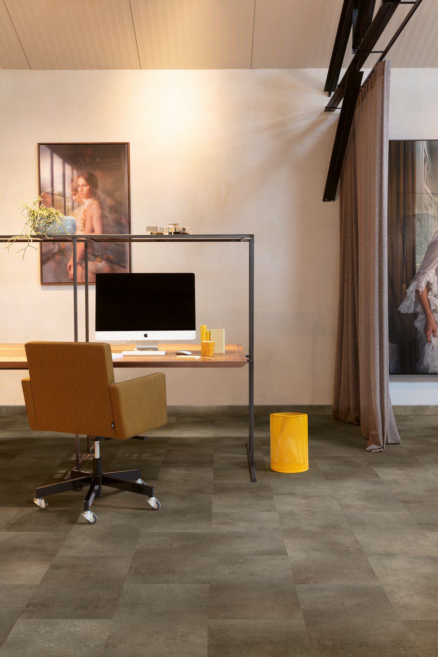 Vinyl Tile flooring Quick-Step Oro Oxidized rock installed on a home office floor. Orange office stool, office working table, paintings on wall.