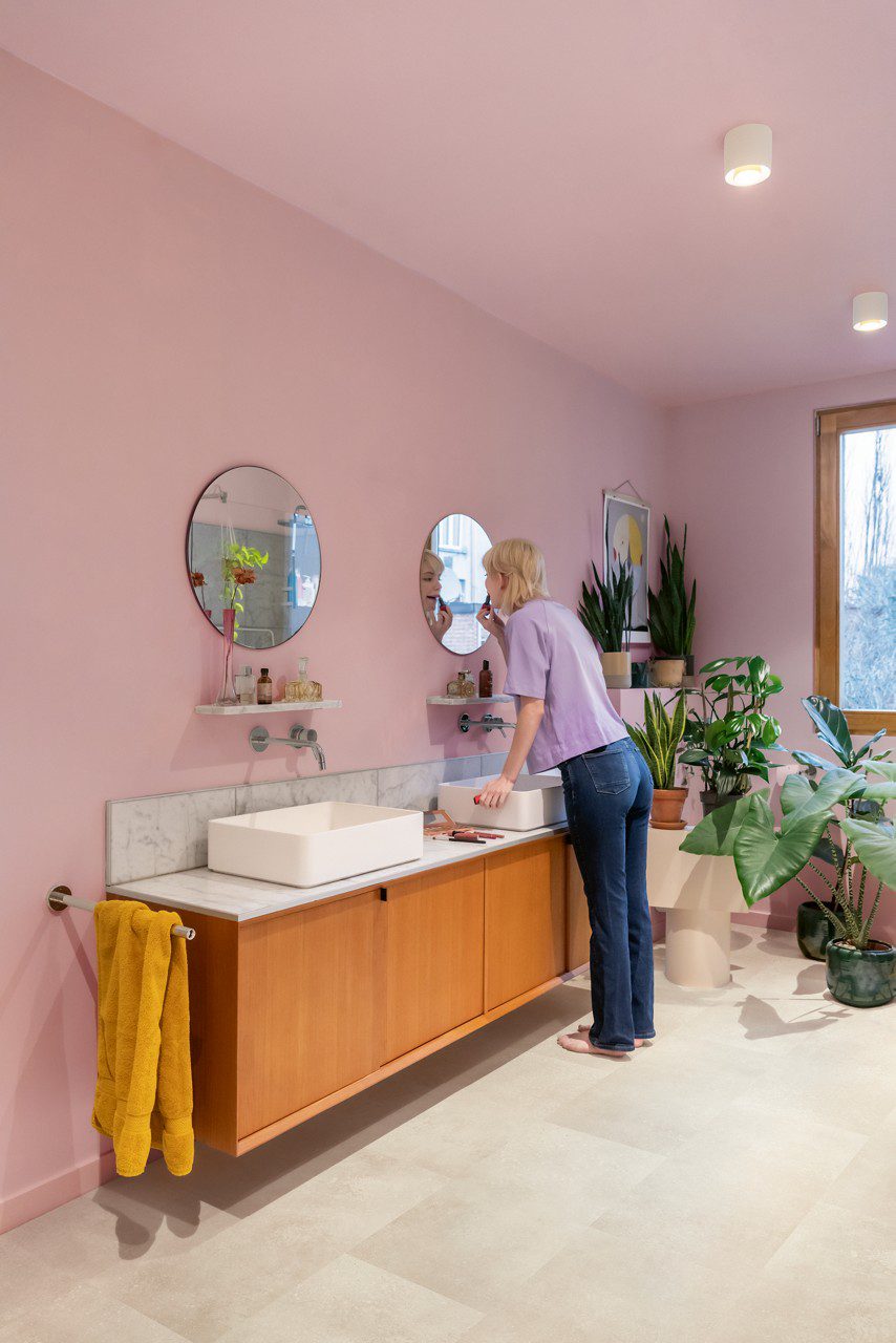 Vinyl tiles Quick-Step-Oro-Coral Rock installed on bathroom floor. Double bathroom furniture and woman washing her teeth looking to mirror.