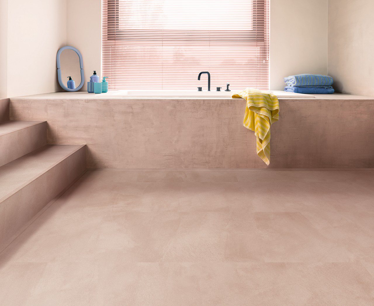 Кварц-винил Quick-Step Illume Soft Blush уложен на полу ванной комнаты и на ступенях лестницы — белая ванна встроена в конструкцию в розовом тоне, совпадающем по оттенку с полом; светлый нежно-розово-бежевый оттенок и спокойный каменно-бетонный дизайн.
