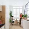 LVT parkett Quick-Step Blos coast tamm sand paigaldatud köögi põrandale. Naine kastab potilille töötasapinnal. Mees istub söögilaua taga ja vaatab telefoni.