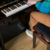 Vinyylilattia Quick Step Bloom Cotton Tammi Natural asennettuna olohuoneen lattialle, luonnollinen tammen sävy ja lankkudesign, joku soittaa pianoa.