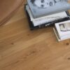 Tammiparketti Bauwerk Boen Casapark tammi 46 Vivo (138 mm), harjattu ja öljyvahattu, asennettuna olohuoneen lattialle – vaaleanruskealla nahalla verhoiltu nojatuoli ja kirjoja lattialla. Luonnollinen Vivo-sävy ja rustiikkinen sorteerus korostavat tammen eläväistä kuviointia.