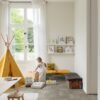 Vinylboden in Steinoptik Quick-Step Oro Concrete Rock, verlegt auf dem Boden eines Kinderzimmers – gelbes Tipi-Zelt im Indianerstil, Spielzeugkiste, Sitzkissen sowie Tisch mit Stühlen; ein Kind nimmt ein Spielzeug aus der Kiste.