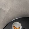Кварц-винил Quick-Step Oro Concrete Rock уложен на полу кухни — кухонный стол, на котором лежат круассан и чашка кофе.