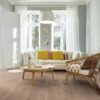 tammiparketti-bauwerk-35-crema-harjattu-bprotect Tammiparketti Bauwerk 35 Crema harjattu B-Protect asennettuna klassistyylisen olohuoneen lattialle – sohva erisävyisillä tyynyillä, nojatuoli, pyöreä sohvapöytä ja suuri valkoinen lattiavalaisin; vaalea, pehmeän lämmin tammen sävy ja luonnollisen rauhallinen puukuvio.